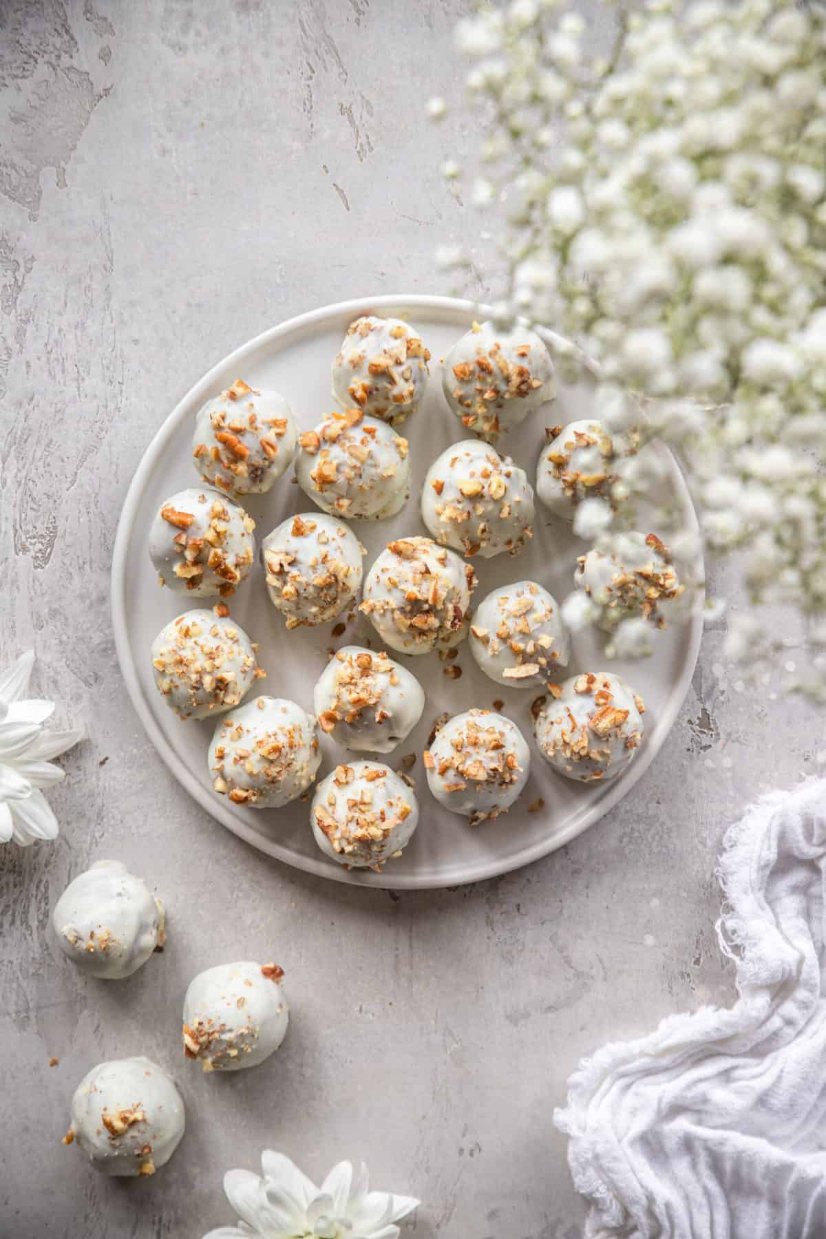 Gluten Free Carrot Cake Truffles - These Gluten Free Carrot Cake Truffles are soft on the inside with a crunchy, sweet candy coating. You'll never know these cute little bites are only 50 calories and better for ya! | #Foodfaithfitness | #glutenfree #carrotcake #healthy #easter Carrot Cake balls on a plate with some flowers